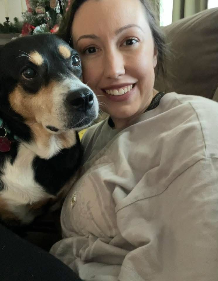 A woman cuddling a tricolor dog on a sofa