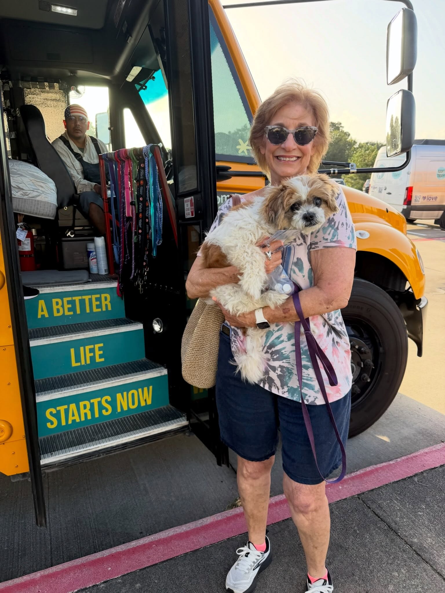 A woman holding a small shaggy dog at the doorway of the yellow rescue bus