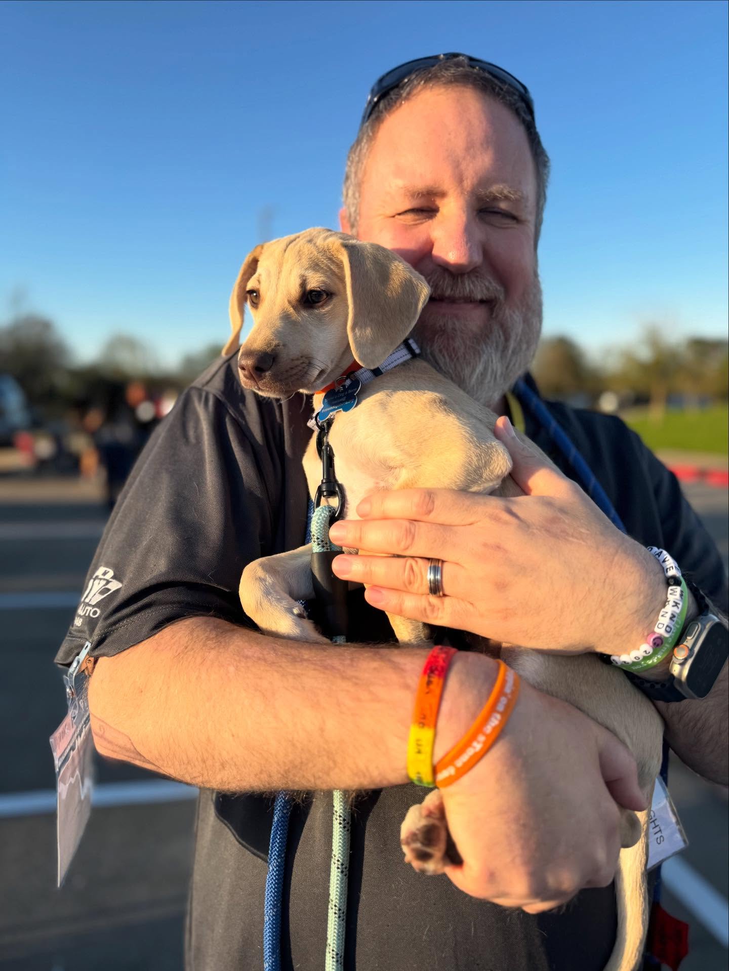 A smiling man hugging a hound puppy outdoors